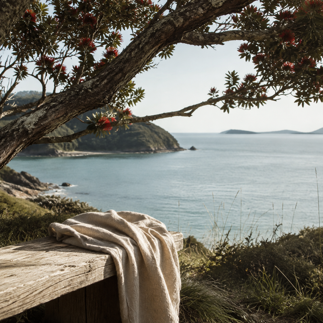 Pōhutukawa overlooking a calm New Zealand coastline with a natural linen scarf in the foreground.