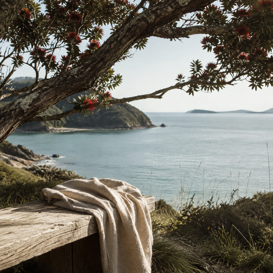 Pōhutukawa overlooking a calm New Zealand coastline with a natural linen scarf in the foreground.